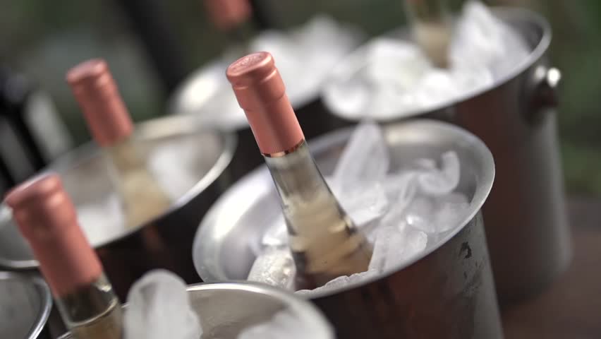 Several champagne white sparkling wine bottles with rose-gold caps nestled in polished stainless steel buckets filled with crystal-clear ice.