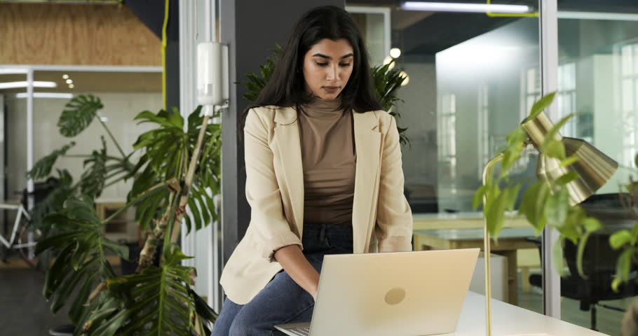 Receiving call alert, Indian woman typing on silver laptop tilting screen, smiling in office lounge. Professional, workspace, modern, lifestyle, business, technology, collaboration