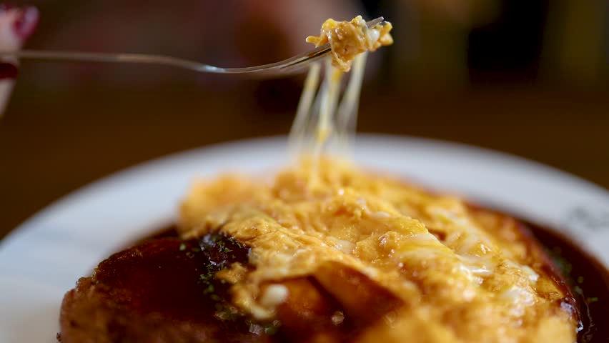 Close-up of fork lifting gooey cheese from omurice with demi-glace, soft natural lighting