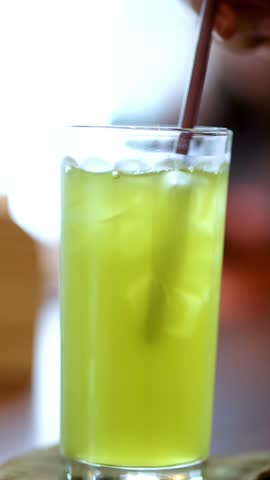 Hand stirs iced green tea with straw in bright, indoor Bangkok dining setting, shallow focus