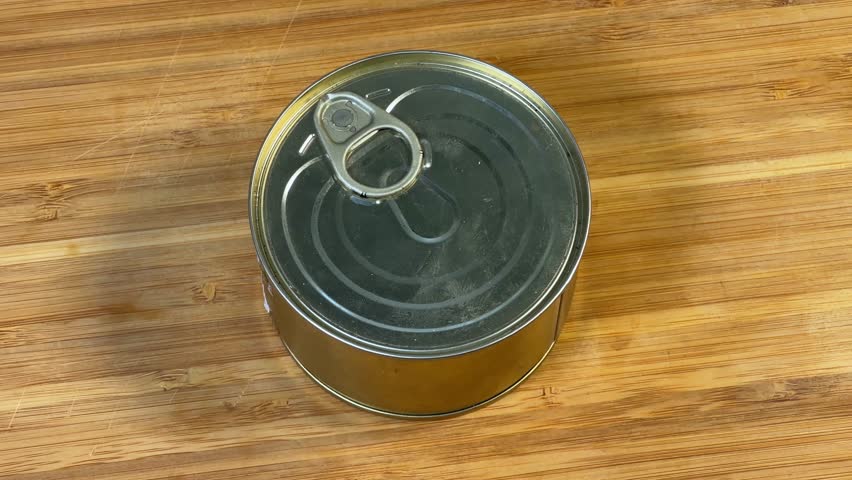 Opening the canned fish in its own juice in tin can with easily opened lid on a wooden cutting board, close-up
