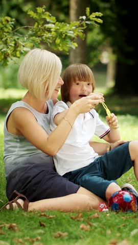 A woman and a boy with down syndrome play and laugh while blowing bubbles in a sunny park They share joy