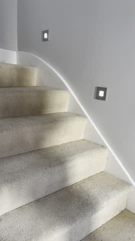 Vertical video - Closeup slow motion shot of a casually dressed man walking up a carpeted and lit staircase in a home.