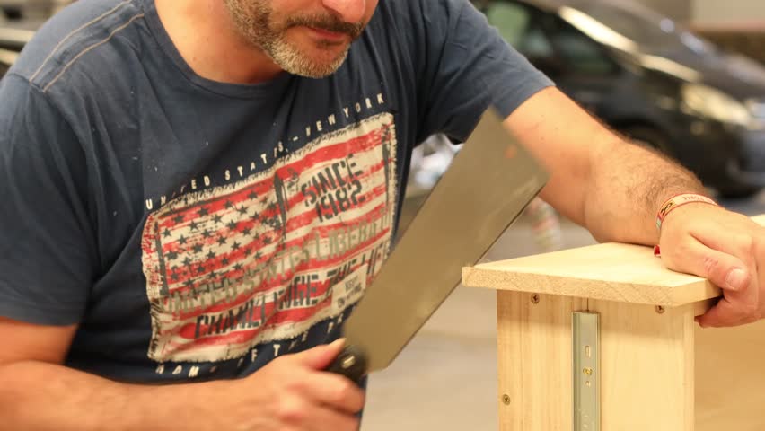 Close-up shot of a craftsman cutting a wooden plank with a hand saw. Only the hands and part of the torso are visible while manually working with precision