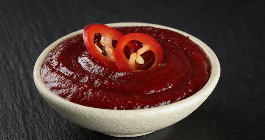 Bowl with spicy gochujang paste and fresh chili pepper slices. Close-up footage on a rotating table.
