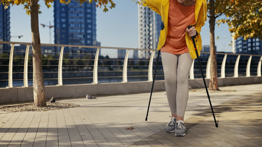 Senior lady feeling back pain while walking with trekking poles, osteoporosis