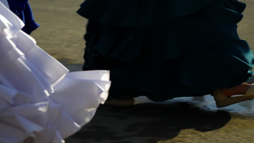 Feet in motion with traditional flamenco dresses dancing on asphalt at Seville fair