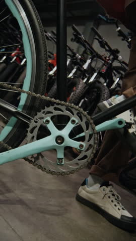 Vertical of unrecognizable man checking used bicycle in shop, turning its pedal, pushing it with foot