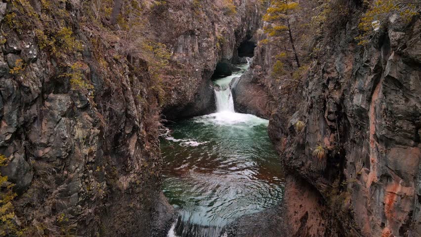 Backward drone aerial of multi-tiered waterfalls through narrow canyon, Siete Tazas National Park, Ñuble, Chile with rugged volcanic rock walls