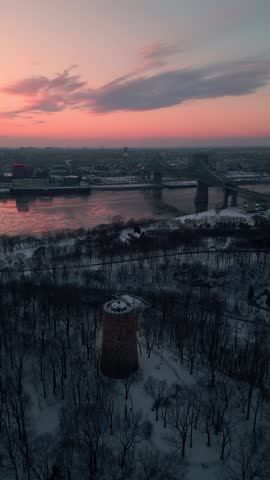 aerial vertical shot around Levis tower in Jean Drapeau Parc with Montreal city in the background at sunset during winter season, Quebec province, anada