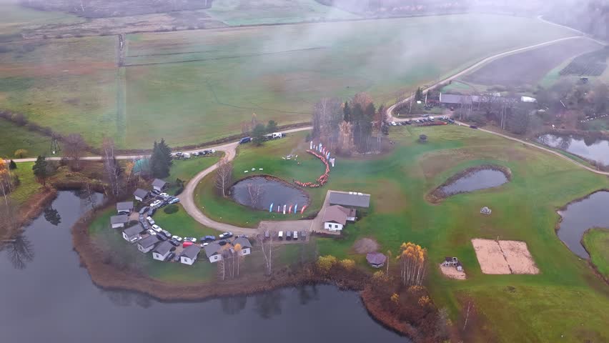 Aerial of a rural lakeside gathering with houses and mist overhead.