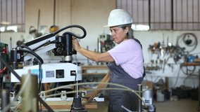 Middle aged female worker in a hard hat and overalls operating a industrial drilling machine in a busy workshop, focusing on her task - Powered by Shutterstock - Get 15% off with code: PIKWIZARD15