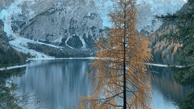 Cinematic view of Lake Braies in the Italian Dolomites with snow-capped mountains and autumn-colored trees. Drone captures serene waters, vibrant fall foliage, and majestic alpine scenery - Powered by Shutterstock - Get 15% off with code: PIKWIZARD15