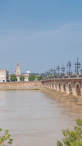 Pont de Pierre timelapse, the historic Stone Bridge in Bordeaux, spans the Garonne River with arches and vintage streetlights. A landmark connecting the city, trams passing by and pedestrians walking