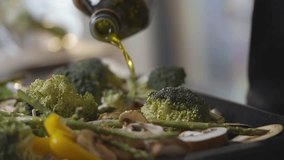 A person is pouring oil over a plate of vegetables. The vegetables include broccoli, mushrooms, and asparagus. The oil is being poured over the vegetables to enhance their flavor - Powered by Shutterstock - Get 15% off with code: PIKWIZARD15