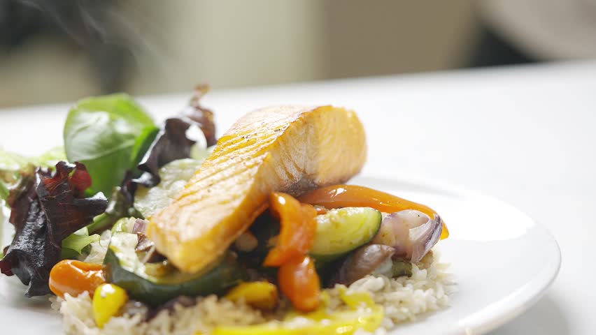 A plate of food with a piece of salmon and vegetables. The plate is white and the food is colorful