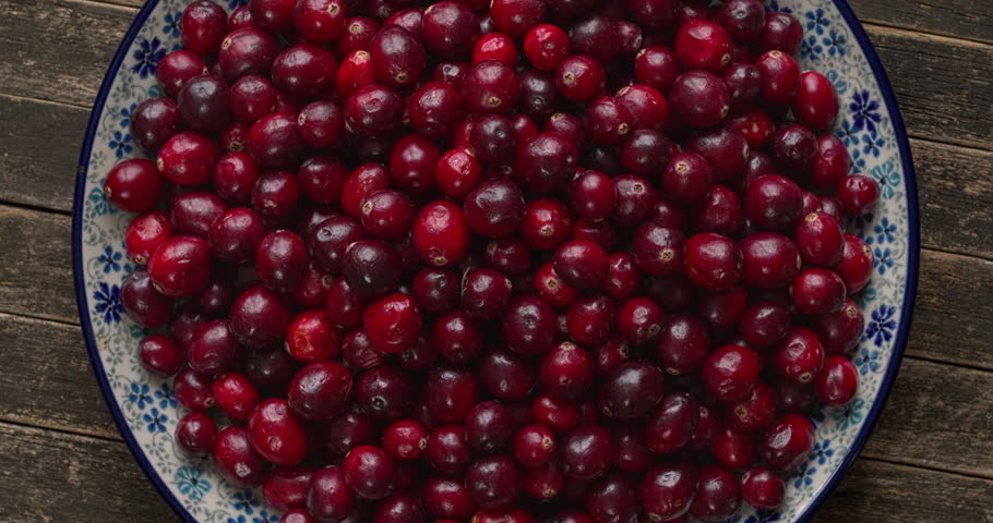 A pile of fresh cranberries on a decorative platter. Rustic wooden background, flat lay, table spin.