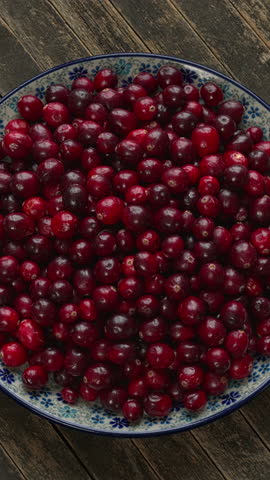 A pile of fresh cranberries on a decorative platter. Rustic wooden background, flat lay, table spin, vertical video.