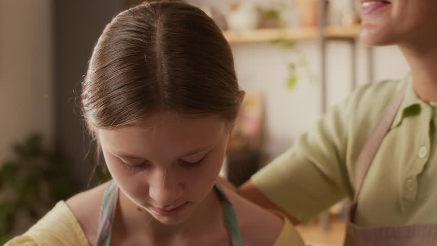 Close up of happy adult woman kissing gently teenage daughter on head while baking pastries together in kitchen, slow motion