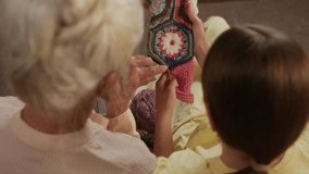 Rear view of elderly woman with grey hair teaching granddaughter knitting with needles explaining crafting technique on woven sweater while spending weekend together at home - Powered by Shutterstock - Get 15% off with code: PIKWIZARD15