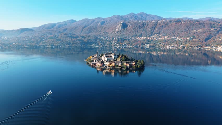 Aerial view of Isola San Giulio, a picturesque island with historic buildings, surrounded by calm waters reflecting the clear blue sky, Isola San Giulio, Piemonte, Italy.
