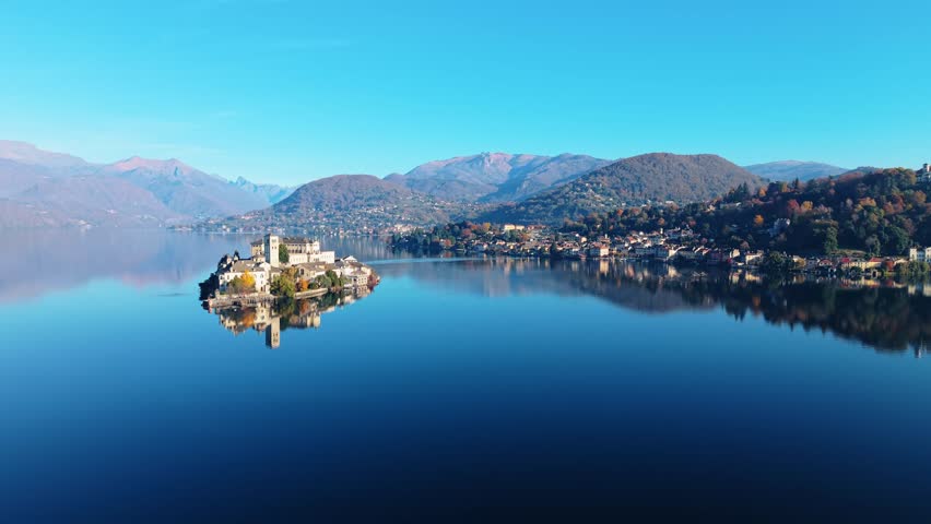 Aerial view of Isola San Giulio island reflecting on the serene water, with mountains in the background, Isola San Giulio, Piemonte, Italy.