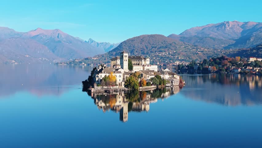 Aerial view of Isola San Giulio, a serene island with historical buildings mirrored in the calm waters of Lake Orta, Isola San Giulio, Piemonte, Italy.