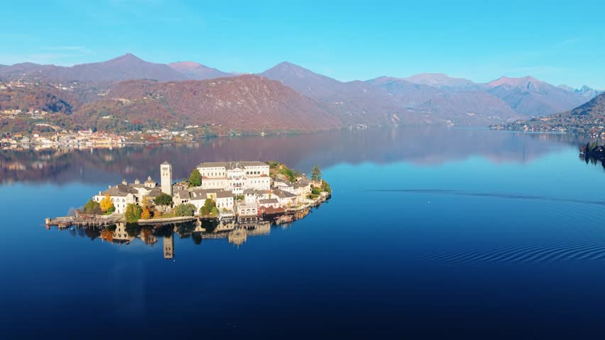 Aerial view of Isola San Giulio island with its buildings reflecting in the still lake waters surrounded by mountains, Isola San Giulio, Piemonte, Italy.