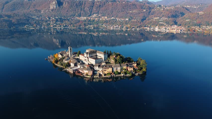 Aerial view of Isola San Giulio island, with its historic buildings casting shadows on the tranquil water, a serene scene of Italian architecture, Isola San Giulio, Piemonte, Italy.
