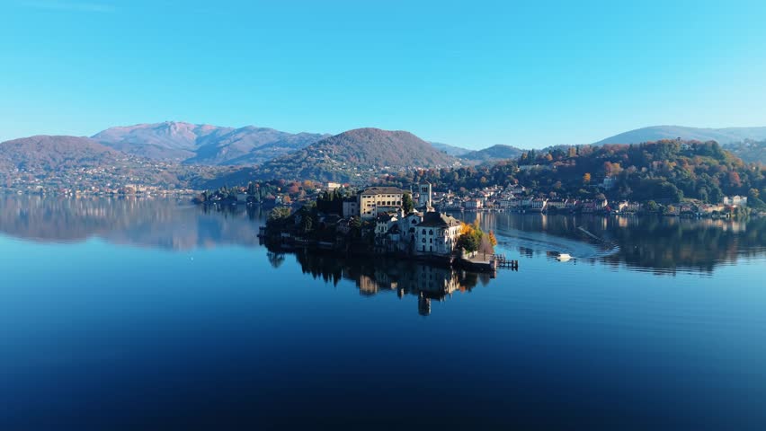 Aerial view of the serene Isola San Giulio reflecting against the tranquil waters under a clear sky, Isola San Giulio, Piemonte, Italy.