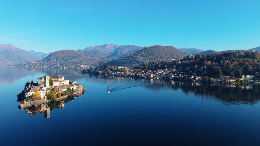 Aerial view of Isola San Giulio, a jewel on Lake Orta, exhibits striking architecture amid still waters, reflecting the crisp, clear sky, Isola San Giulio, Piemonte, Italy.