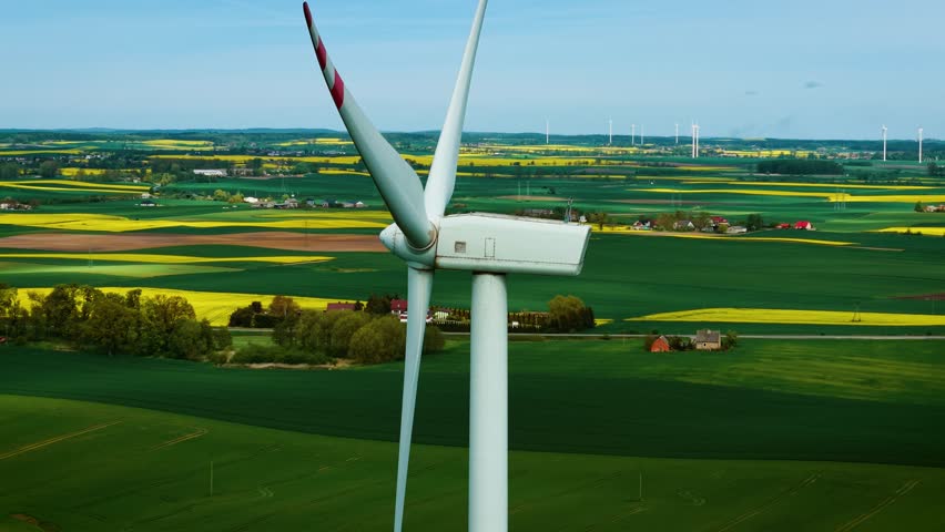 Wind turbine turning above farmland promoting concept of environmental conservation close-up. Wind generator spinning across colorful fields producing sustainable energy. Windmill rotating over