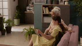 Smiling elderly woman with grey hair waving hand while video calling relatives with teenage granddaughter holding digital tablet, sitting on couch in cozy living room - Powered by Shutterstock - Get 15% off with code: PIKWIZARD15