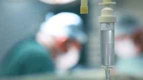 Intravenous drip in a surgical setting, with surgeons working in the background, highlighting medical care and hospital procedures. - Powered by Shutterstock - Get 15% off with code: PIKWIZARD15