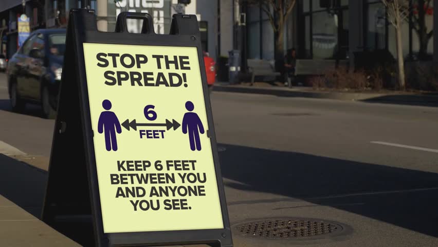 A sidewalk sign in a large city reminds pedestrians to stay six feet apart, illustrating social distancing guidelines commonly practiced during the 2020 COVID-19 pandemic.