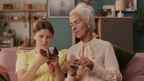 Grey haired elderly woman teaching granddaughter needle knitting showing technique on wool workpiece while sitting on couch in living room spending time together - Powered by Shutterstock - Get 15% off with code: PIKWIZARD15