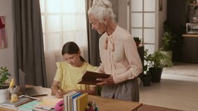 Teenage girl discussing homework task with elderly white haired grandmother pointing at laptop screen and holding coursebook in cozy room - Powered by Shutterstock - Get 15% off with code: PIKWIZARD15