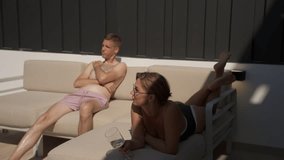 Man and woman enjoy vacation while lounging on comfortable outdoor sofa, woman hold glass of white wine as they both soak up  sun and relax on patio during warm day - Powered by Shutterstock - Get 15% off with code: PIKWIZARD15