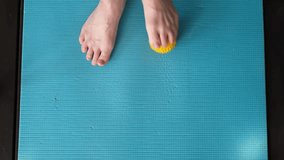 Female feet are doing foot exercises by rolling a prickly massage yellow ball under the foot on the yoga mat pressing down in different sides. Training to correct and relax the foot fascia. 4k footage - Powered by Shutterstock - Get 15% off with code: PIKWIZARD15