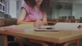 Female student writing notes to study, glancing tablet causing drifting charts and globe icons. Library, woman, focus, concentration, education, digital, overlays - Powered by Shutterstock - Get 15% off with code: PIKWIZARD15