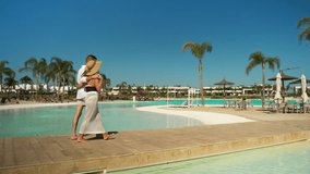 Affectionate young couple strolling arm in arm along wooden poolside boardwalk at luxury tropical resort, palm trees and clear blue sky framing their romantic getaway - Powered by Shutterstock - Get 15% off with code: PIKWIZARD15
