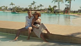 Stylish young couple relaxing together on edge of beautiful swimming pool at luxury tropical resort, enjoy their summer holiday in sun with palm trees in background - Powered by Shutterstock - Get 15% off with code: PIKWIZARD15