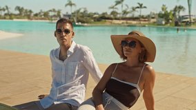 Young elegant couple relaxing on wooden deck by beautiful turquoise swimming pool at tropical resort, enjoying their summer vacation together under  bright sun - Powered by Shutterstock - Get 15% off with code: PIKWIZARD15