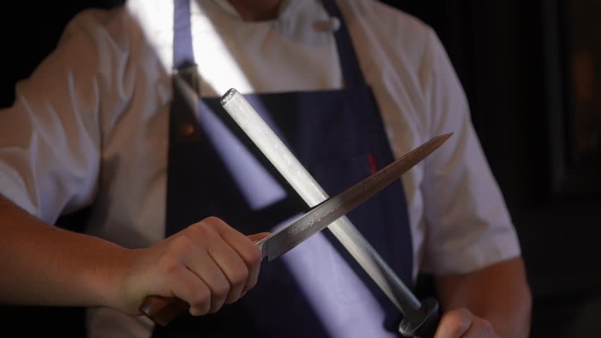 A chef is holding a knife and preparing to cut something. The knife is sharp and the chef is wearing an apron
