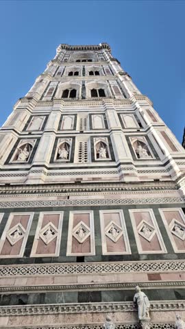 Vertical upward pan of Giotto Bell Tower in Florence, Italy, showcasing its marble facade and Gothic architecture under a clear blue sky.