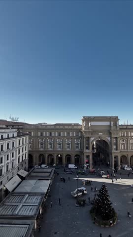 Vertical panoramic view of Piazza della Repubblica in Florence, Italy, with Christmas tree, carousel, and classic architecture under a clear winter sky.