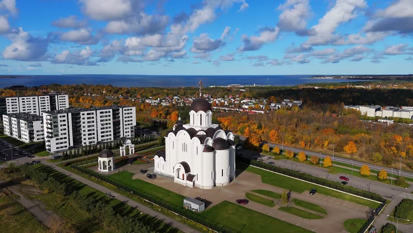 Stunning drone view of an Orthodox church surrounded by autumn colors and modern buildings near the Baltic Sea coastline in Tallinn, Estonia.