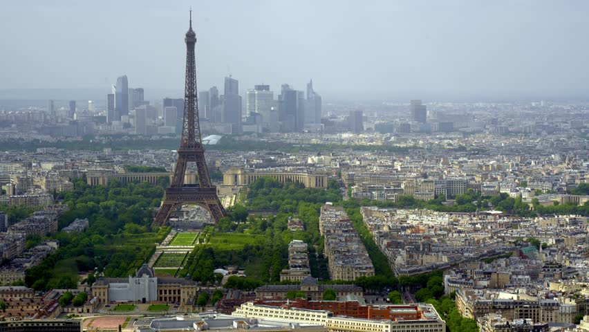 Breathtaking aerial view of the Eiffel Tower and Champ de Mars gardens with the modern La Defense business district in the hazy background, showcasing the vast urban landscape of Paris