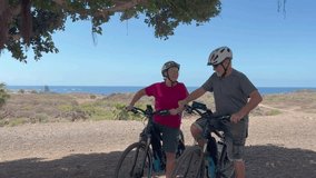 Caucasian senior couple of cyclists wearing helmets enjoying healthy lifestyle riding with electric bicycles in a sunny day. Authentic senior retired life concept. Horizon over the sea - Powered by Shutterstock - Get 15% off with code: PIKWIZARD15