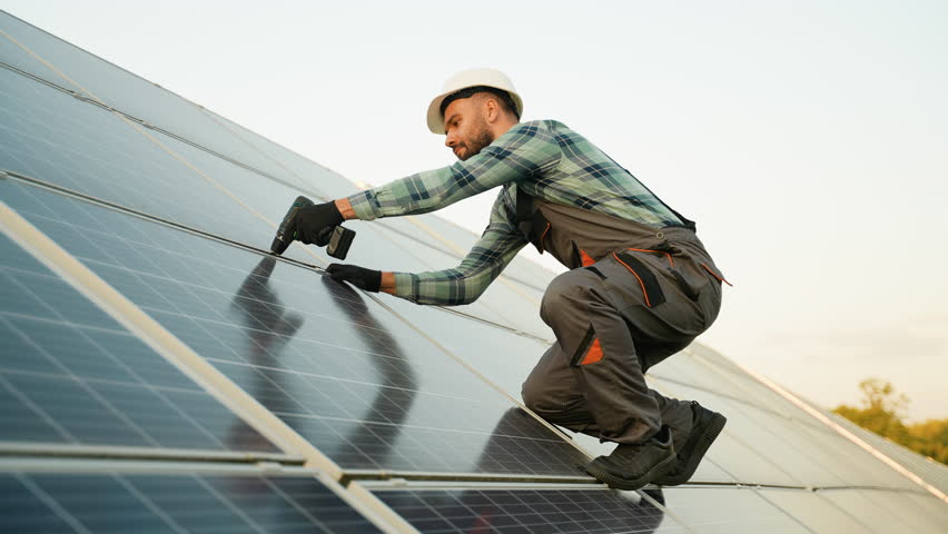 Male technician installing solar panels on roof